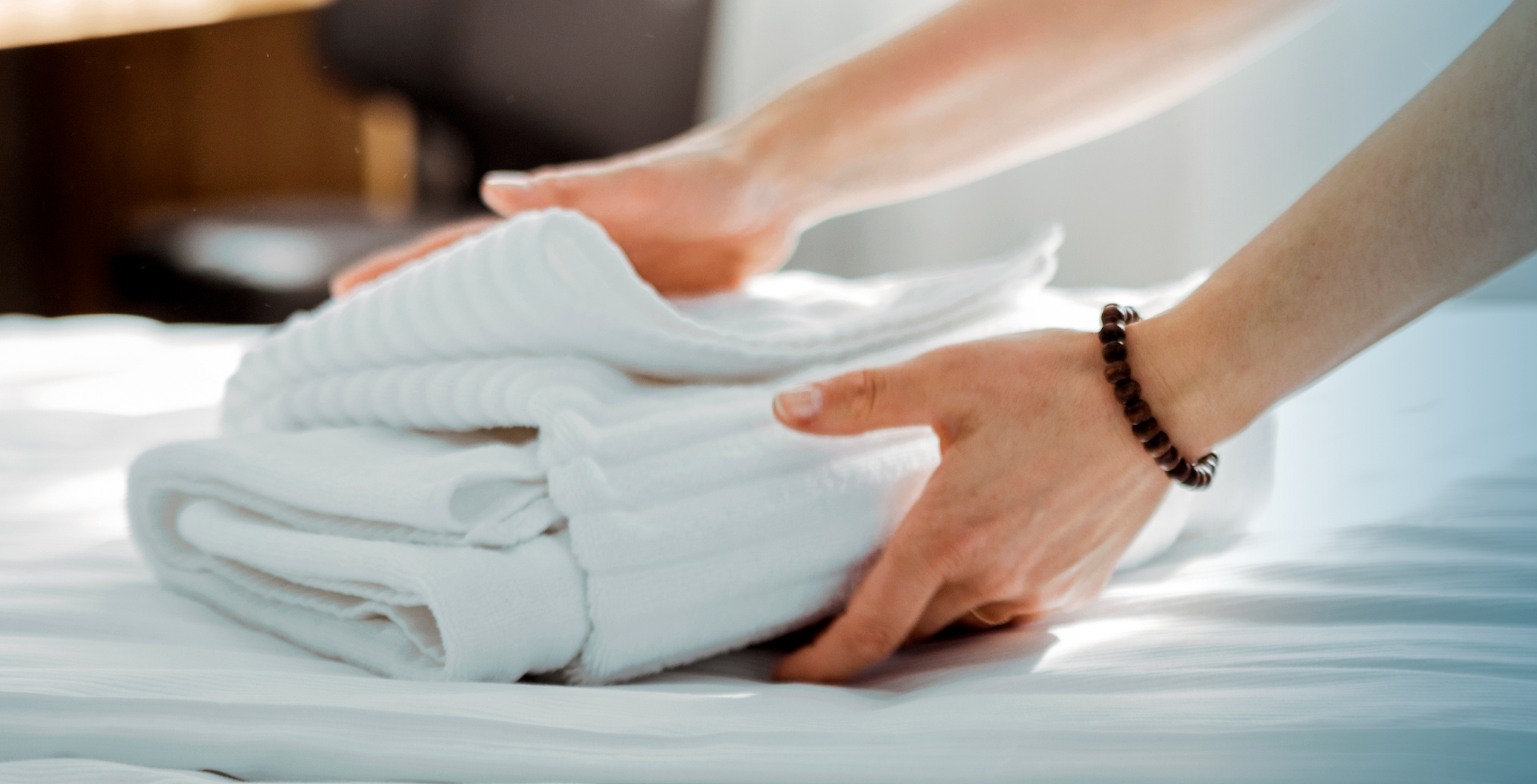 Hände legen einen Stapel Handtücher auf ein Hotelbett