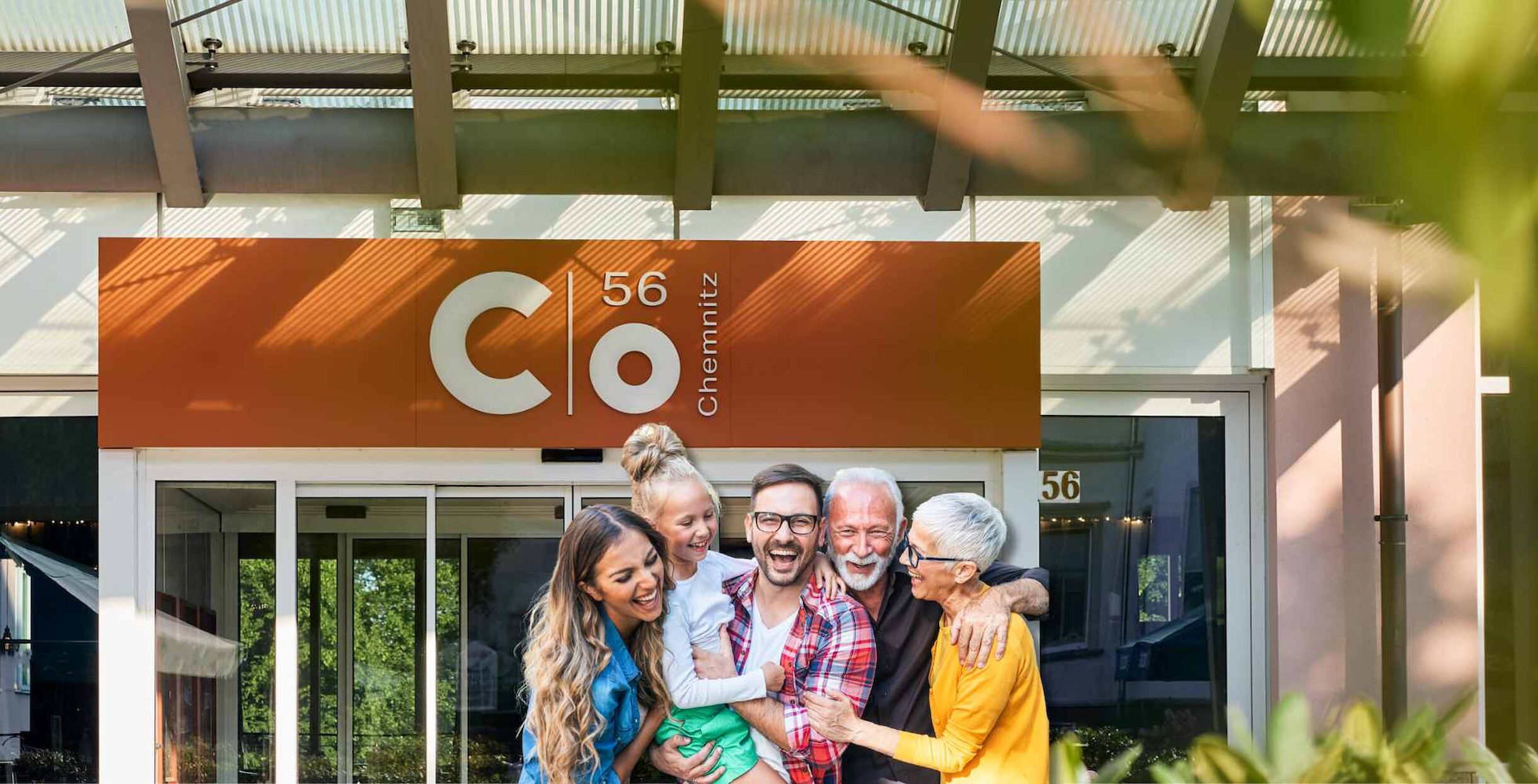Lachende Familie mit Großeltern vor dem Eingang zum Hotel c/o56